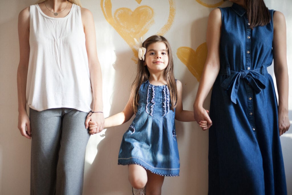 Lesbian couple posing in front of the wall with their adorable little daughter