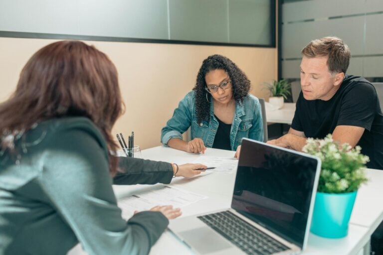 A couple sits at a desk with a corporate professional reviewing documents.